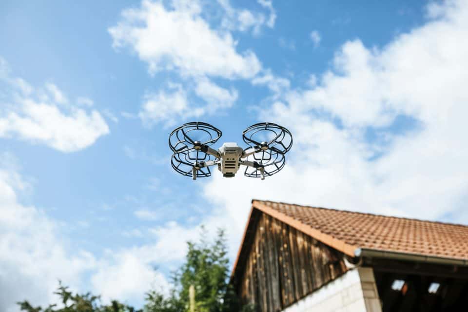 Drone in cloudy sky over building and trees